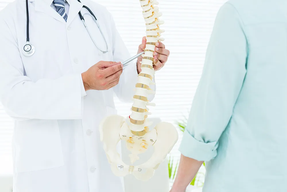 脊椎模型を持って患者に説明する医師